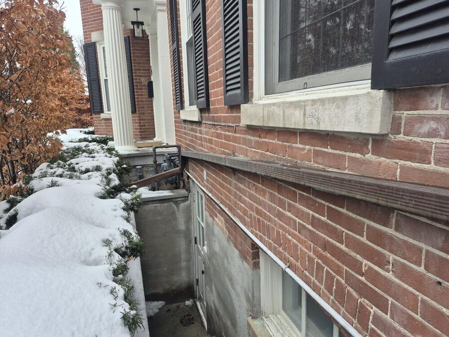 Worn horizontal downspout along a brick wall before replacement